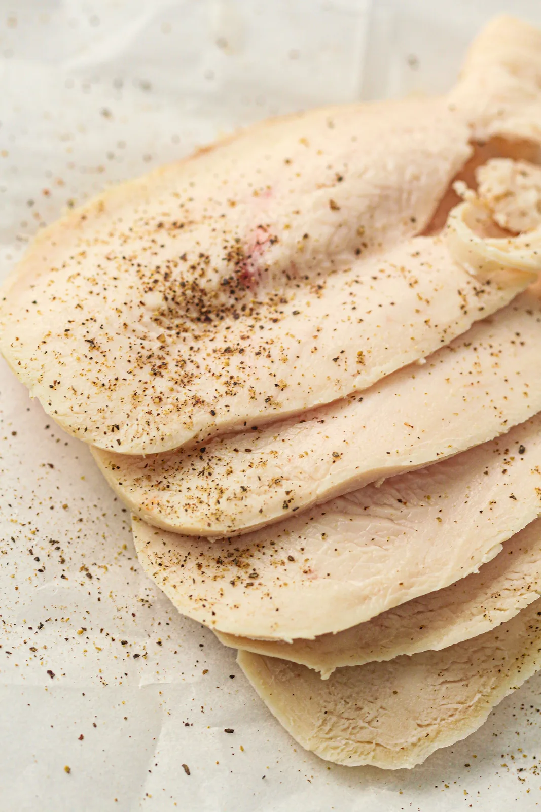 Homemade deli meat sliced thinly and stacked on parchment paper with black pepper