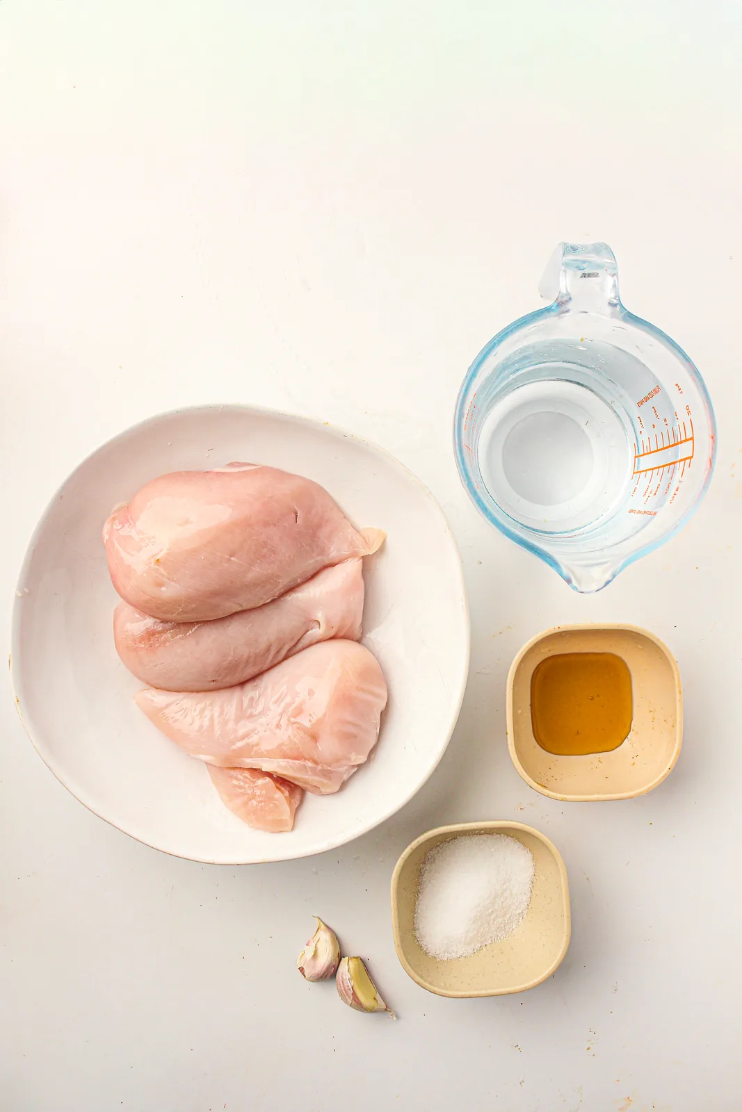 Ingredients for homemade deli meat: raw chicken breasts, water, salt, honey and garlic cloves