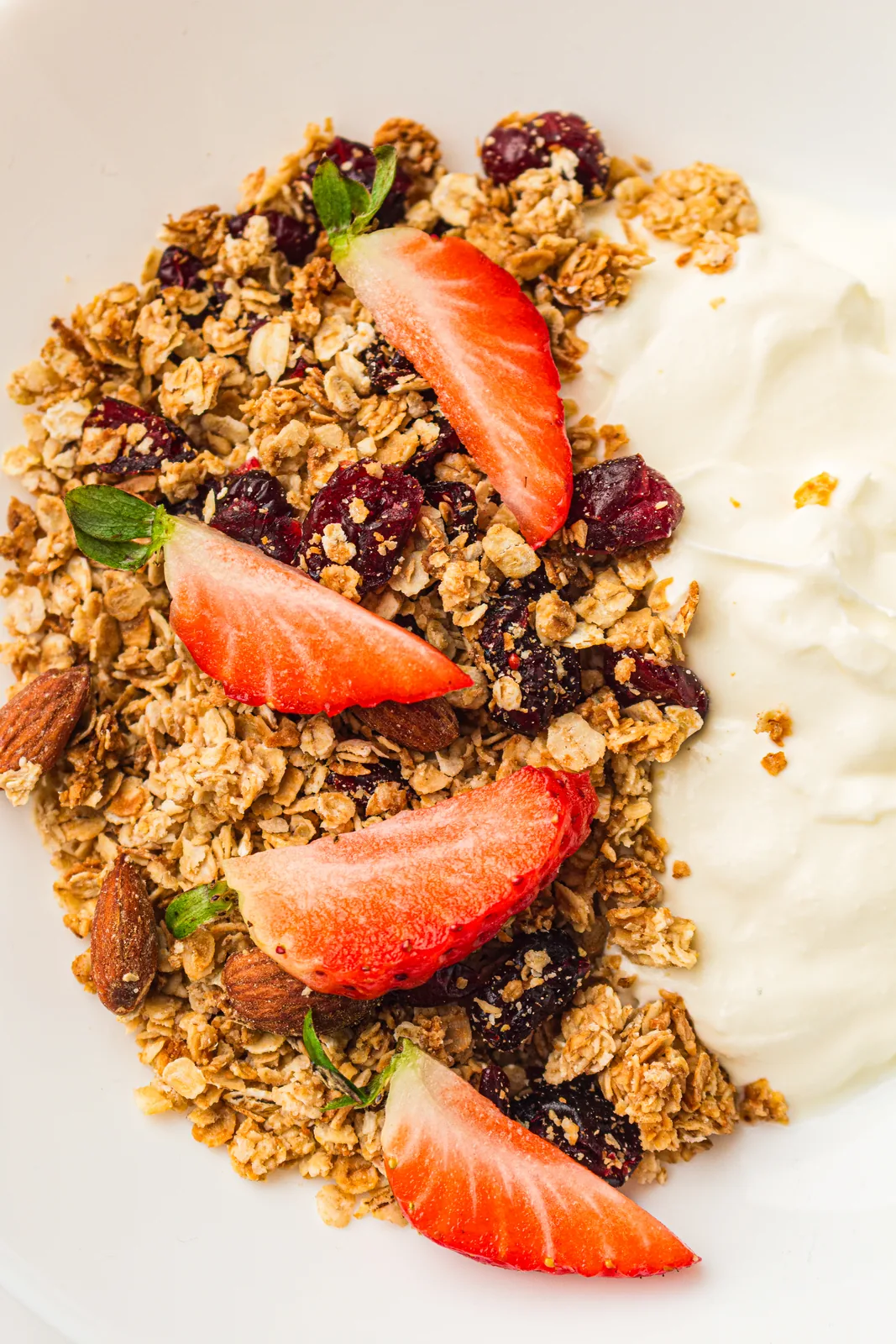 Homemade granola with cranberries and almonds served beside thick yoghurt and fresh strawberries
