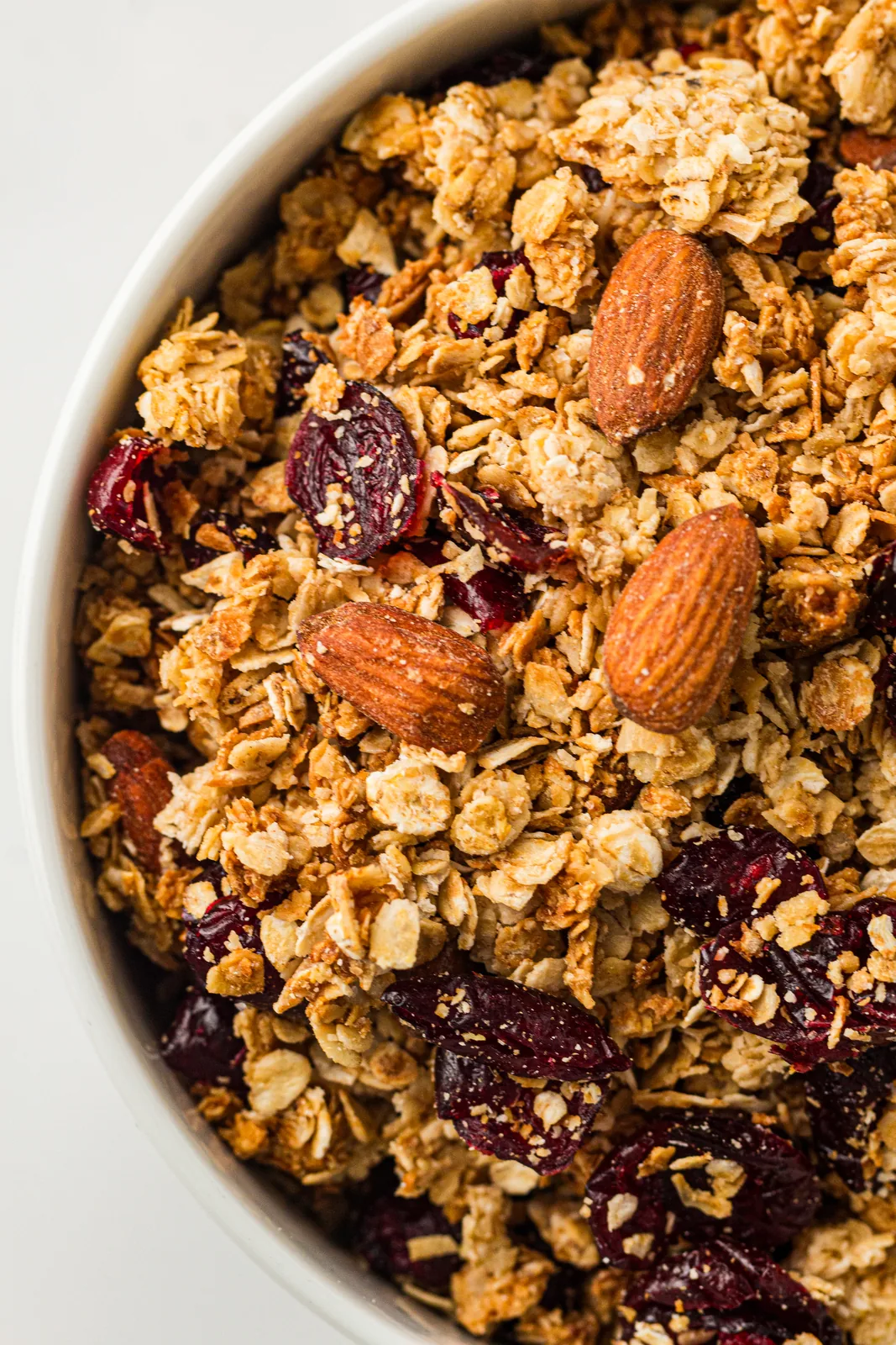 A white bowl of golden oat clusters with whole almonds and dried cranberries