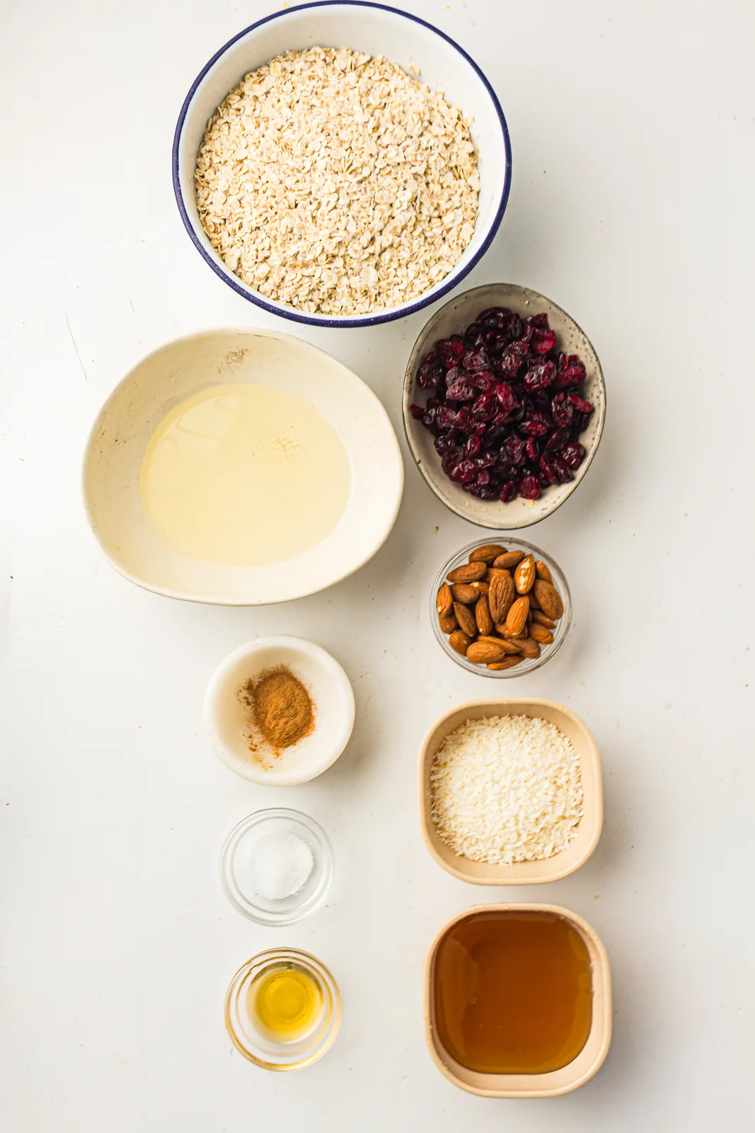 Ingredients for homemade granola: rolled oats, almonds, coconut, cranberries, maple syrup, oil, cinnamon and salt