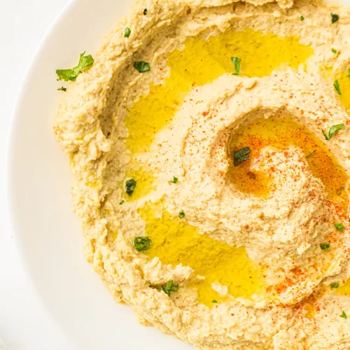 Creamy hummus swirled in a white bowl with olive oil and paprika
