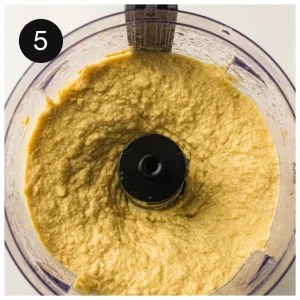 A thick chickpea paste being blended in a food processor