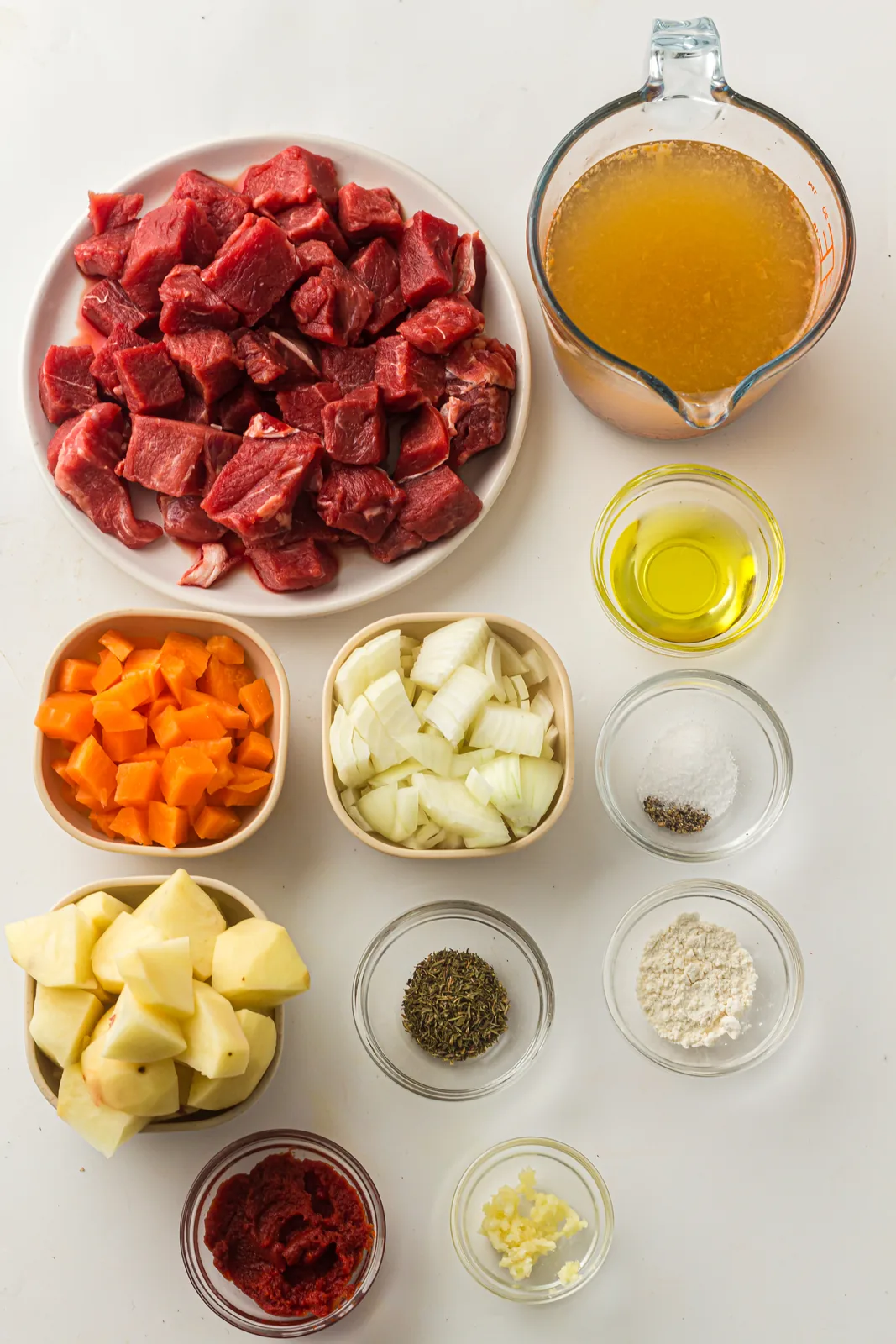 Ingredients for instant pot beef stew: cubed chuck, carrots, potatoes, onion, broth and tomato paste