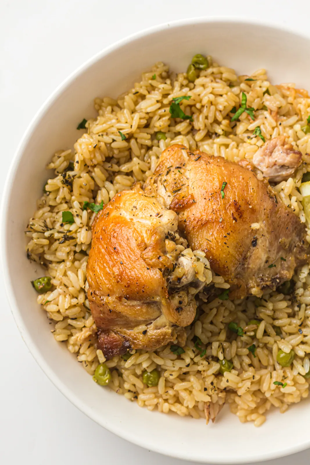 Instant pot chicken and rice in a white bowl, browned thigh sitting on fluffy seasoned rice