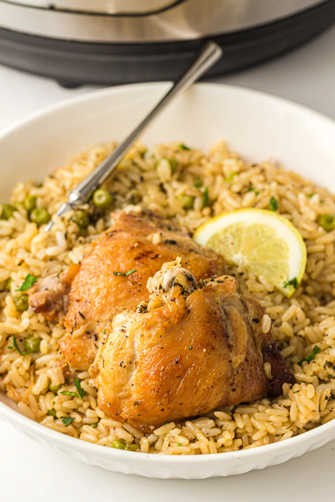 A shallow bowl of seasoned grains and golden thighs with a lemon wedge, pressure cooker behind