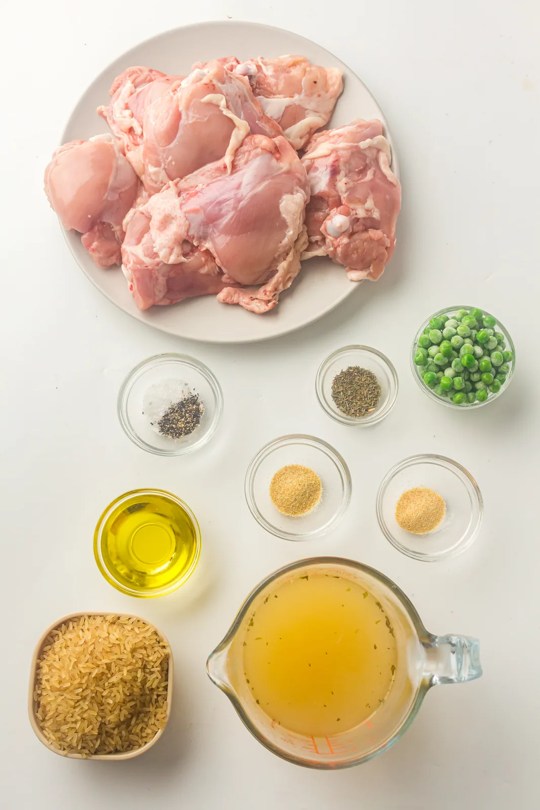 Ingredients for instant pot chicken and rice: bone in thighs, long grain rice, broth, peas and pantry spices