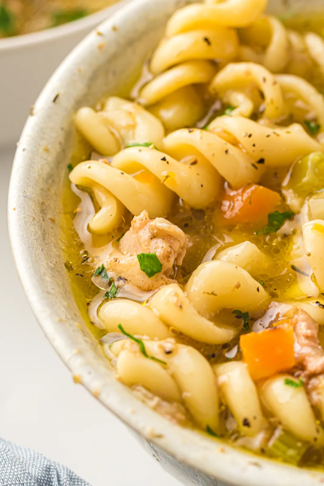 Instant pot chicken noodle soup in a speckled bowl with fusilli, carrot and celery