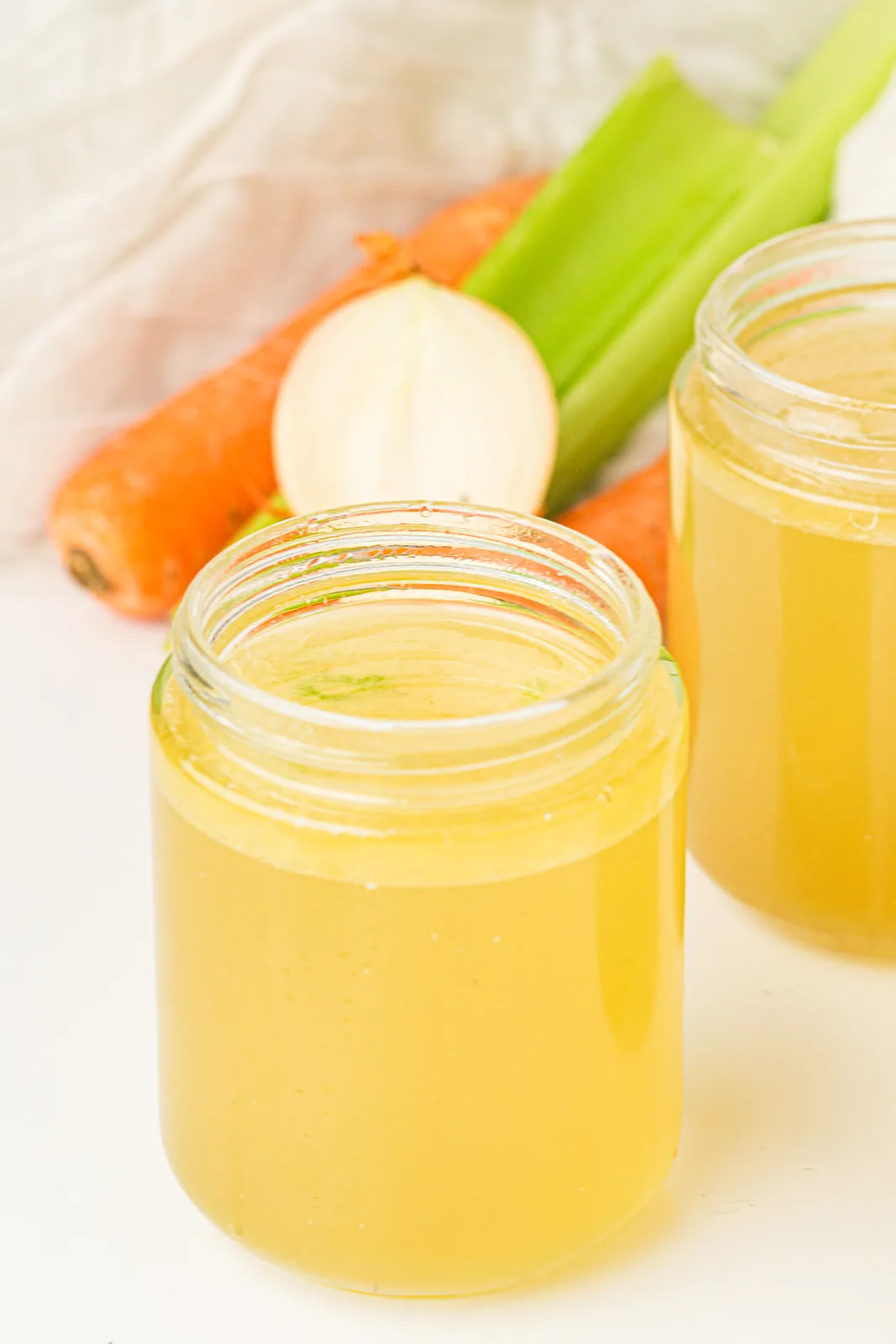 Instant pot chicken stock in a glass jar, golden and clear, with carrot and onion beside it