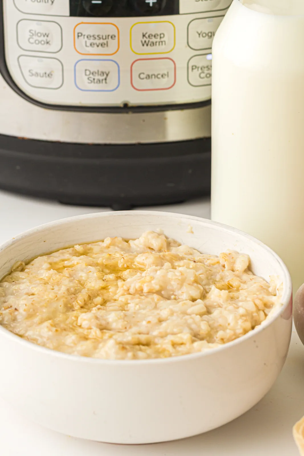 Instant pot oatmeal in a white bowl in front of the pressure cooker