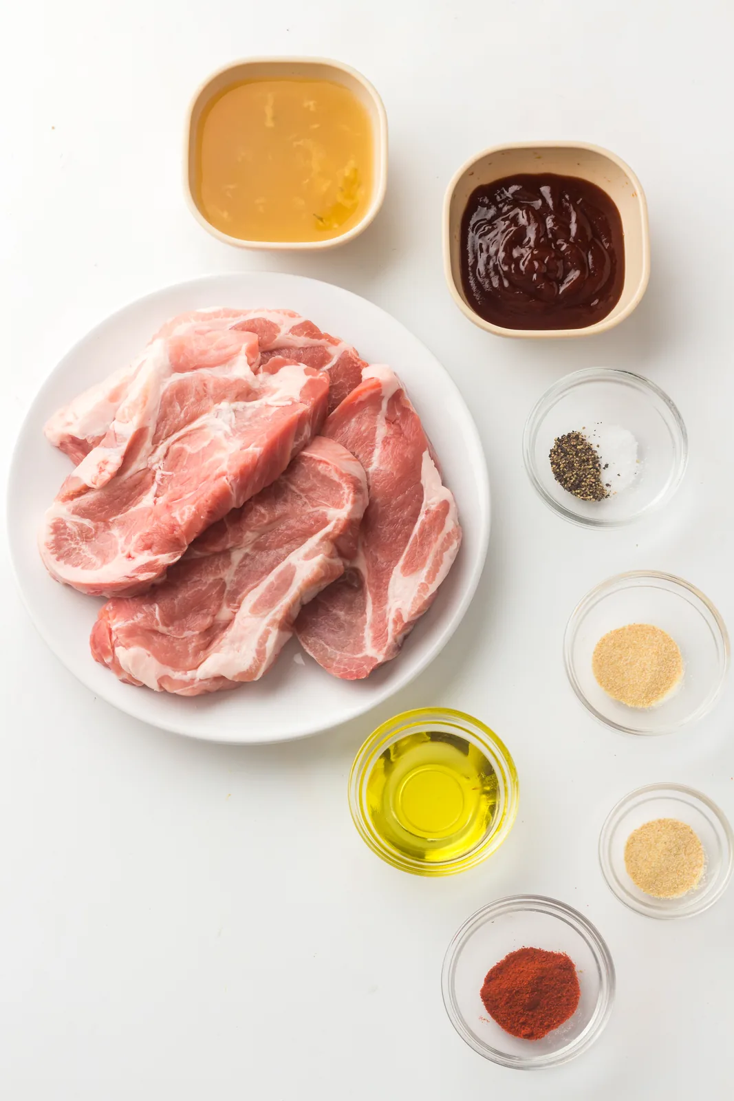 Ingredients for instant pot pulled pork: raw shoulder steaks, barbecue sauce, broth, oil and dry spices