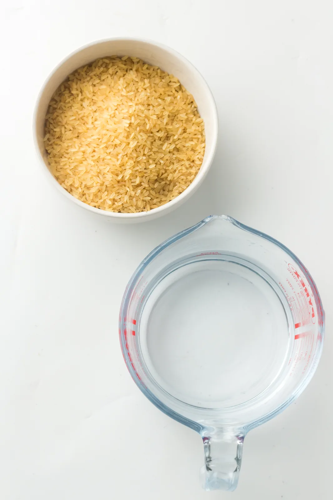 Ingredients for instant pot white rice: a bowl of long grain rice and a measuring jug of water