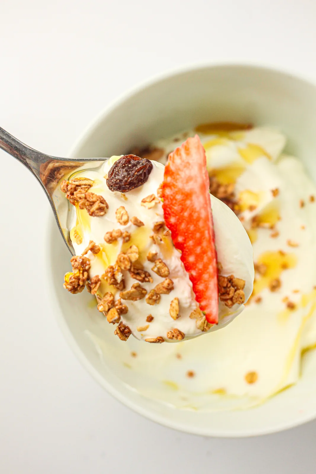 A spoonful of thick creamy dairy lifted from the bowl with fruit and granola
