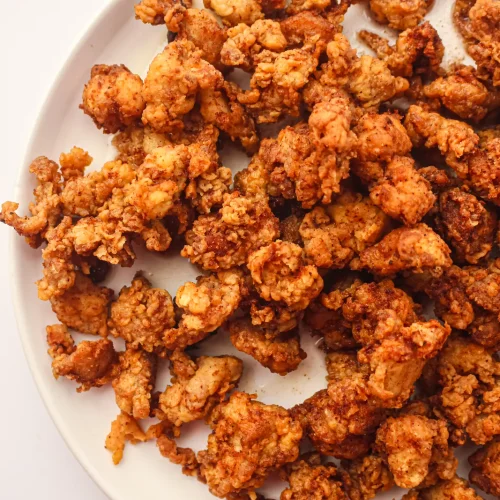 Popcorn chicken piled on a white plate, deep golden and crunchy