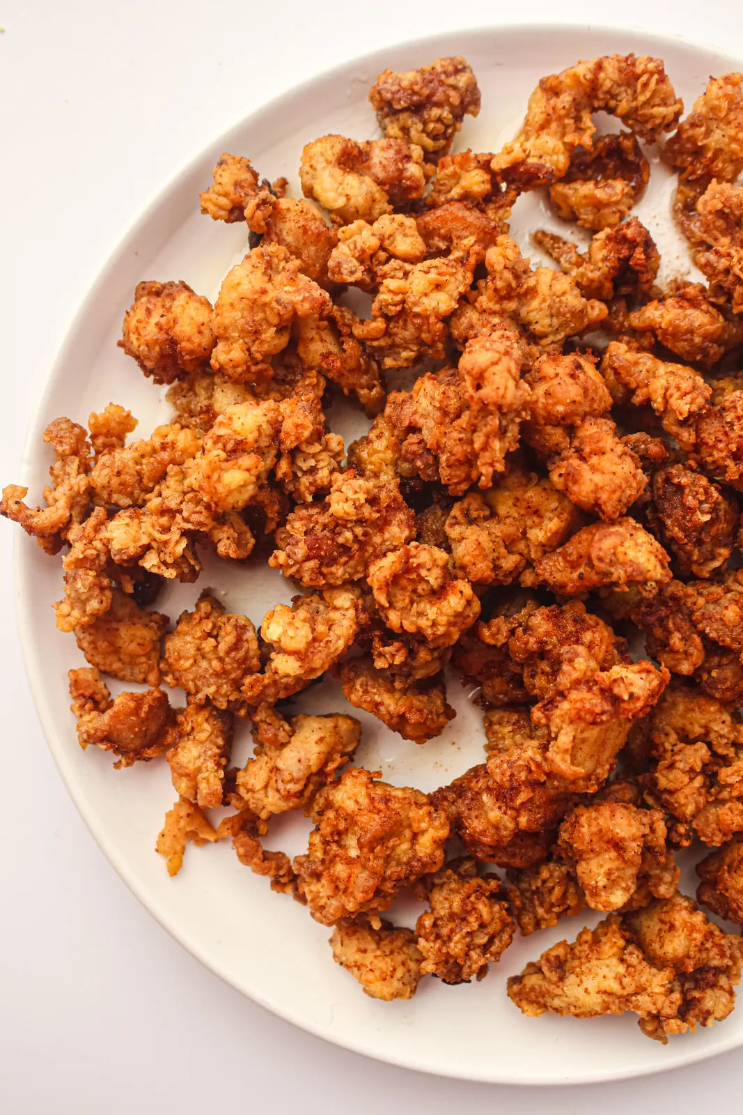 Popcorn chicken piled on a white plate, deep golden and crunchy