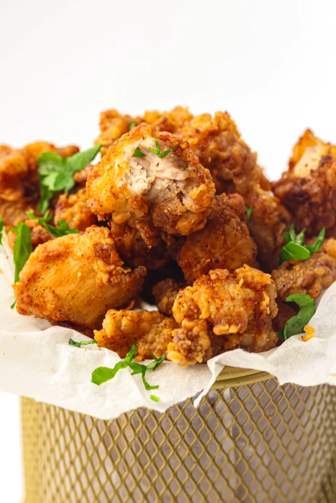 Golden crunchy bites piled into a lined metal basket with parsley scattered over