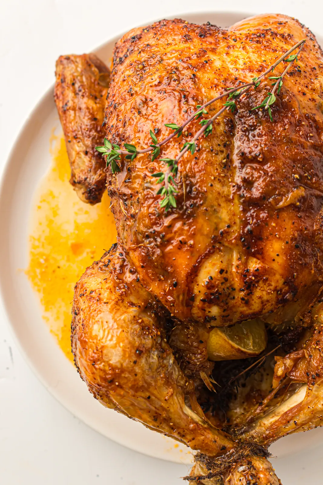 Whole golden roasted bird with crisp, peppery skin and sprigs of thyme on a white plate