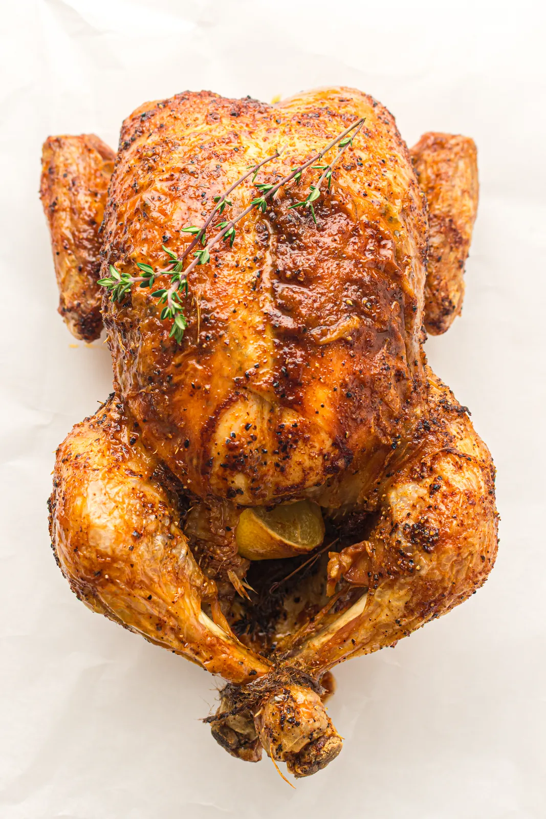 Whole roast chicken on a white platter with thyme and buttery pan juices