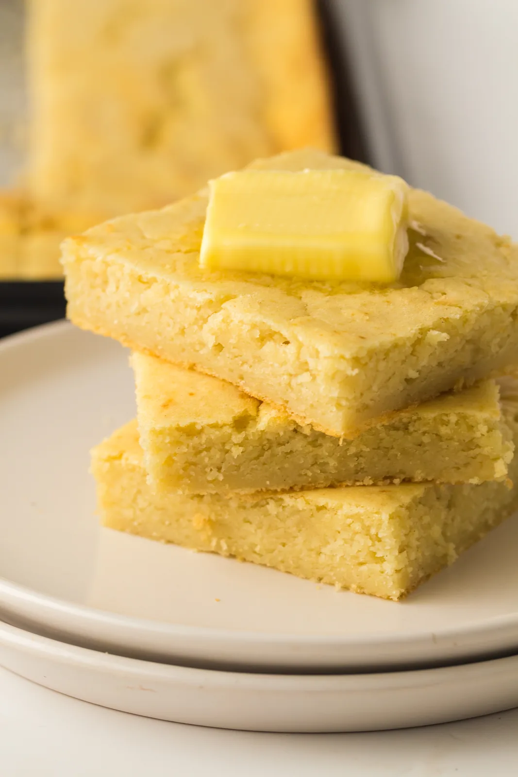 A stack of soft golden squares on a plate with a pat of butter melting on top