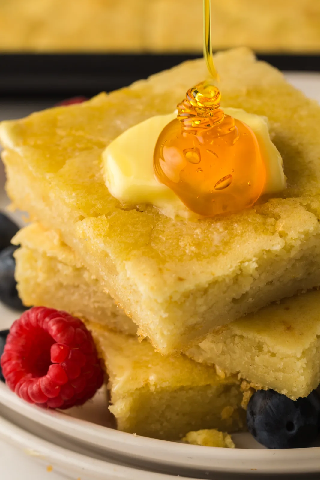 A stack of golden squares with butter and honey running down the sides