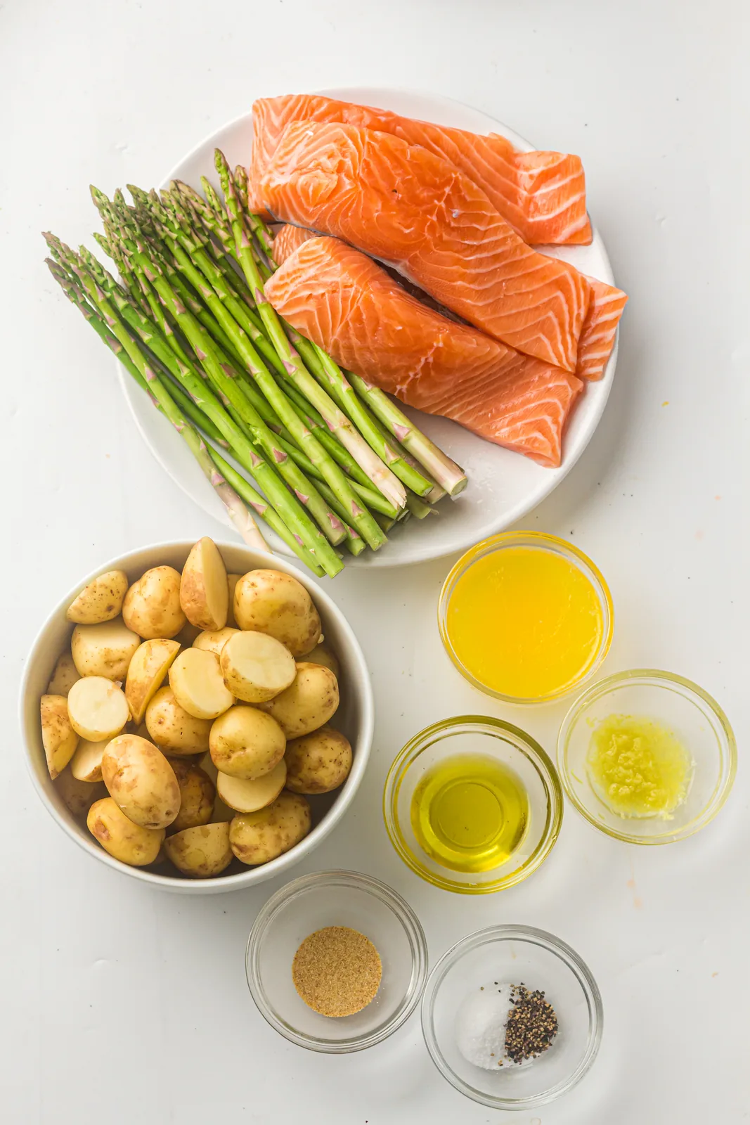 Ingredients for sheet pan salmon: fillets, baby potatoes, asparagus, olive oil, butter, lemon, garlic powder and seasoning