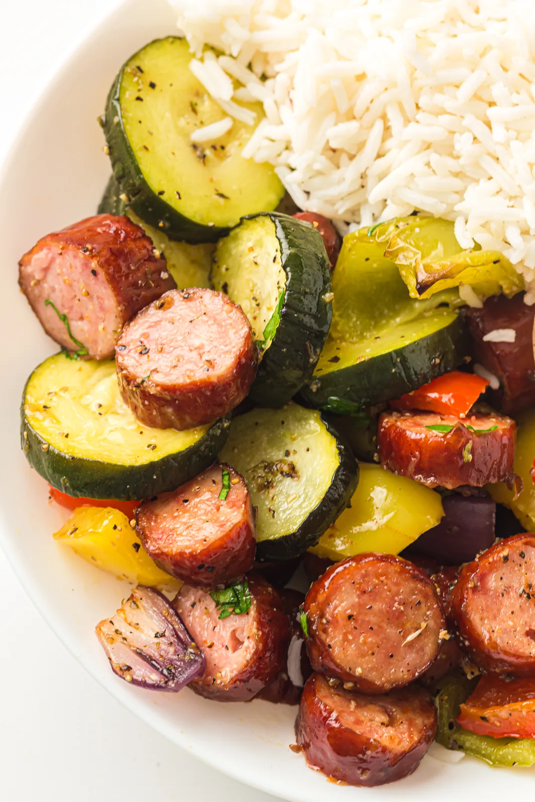 Sheet pan sausage and vegetables served in a white bowl with rice