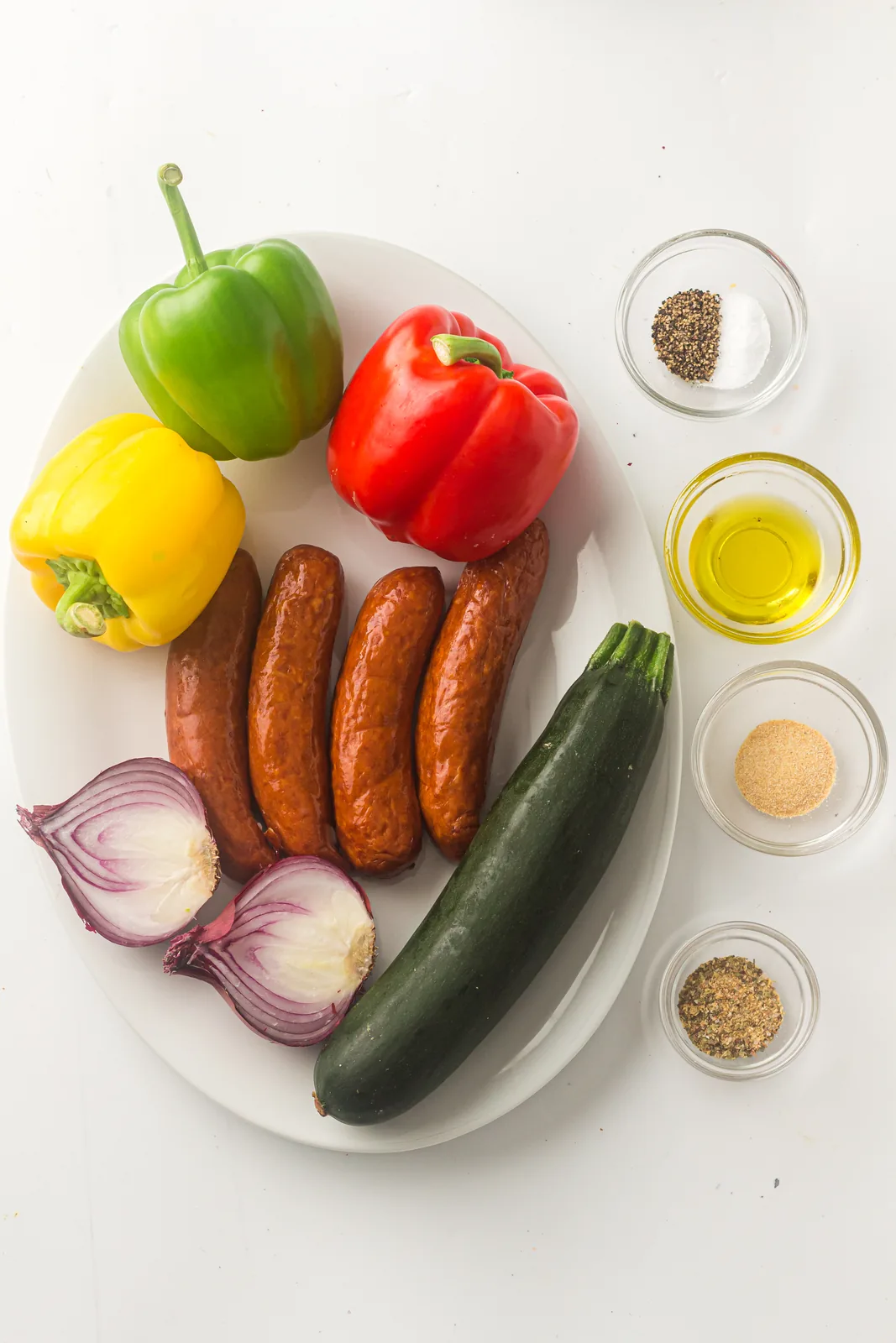 Ingredients for sheet pan sausage and vegetables: smoked sausages, three bell peppers, courgette, red onion, olive oil and seasoning