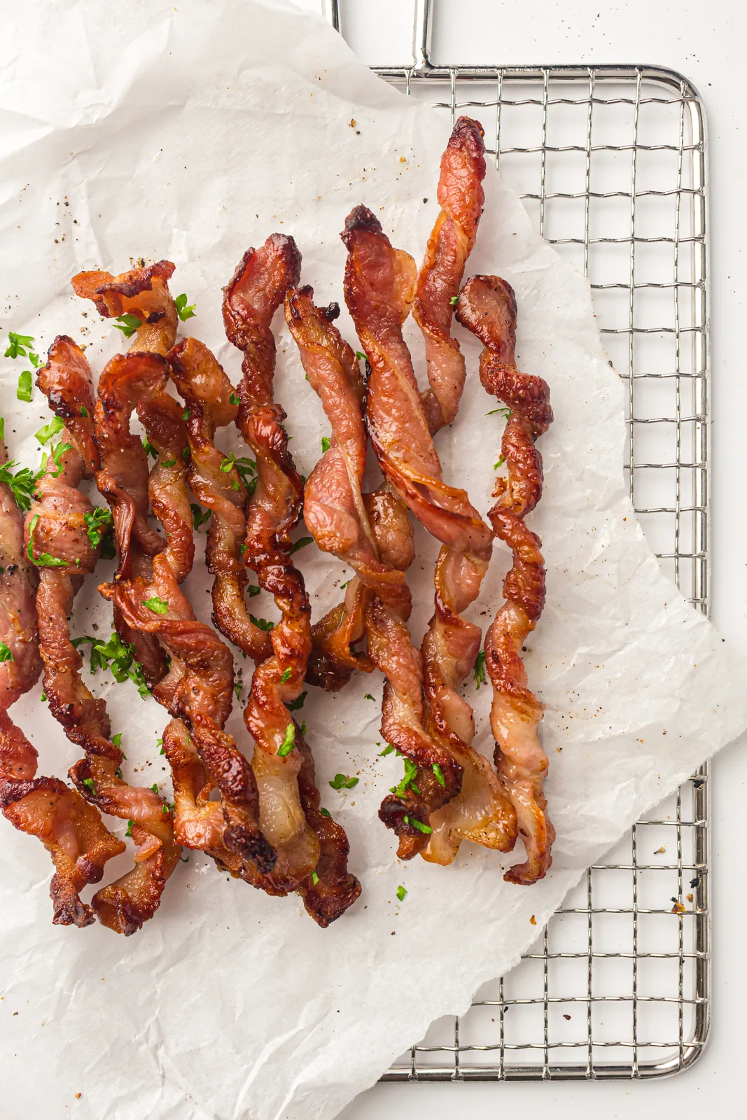 Twisted bacon spirals cooling on parchment beside a wire rack, scattered with parsley