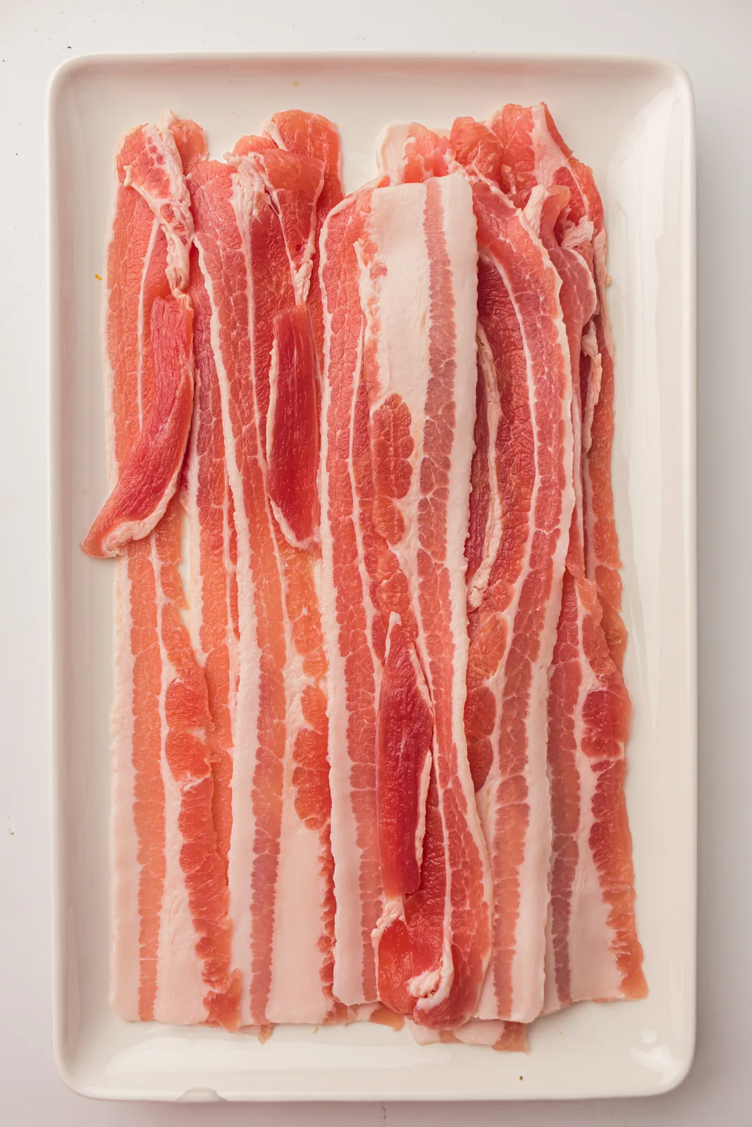 Ingredients for twisted bacon: nine raw streaky rashers laid out on a white tray