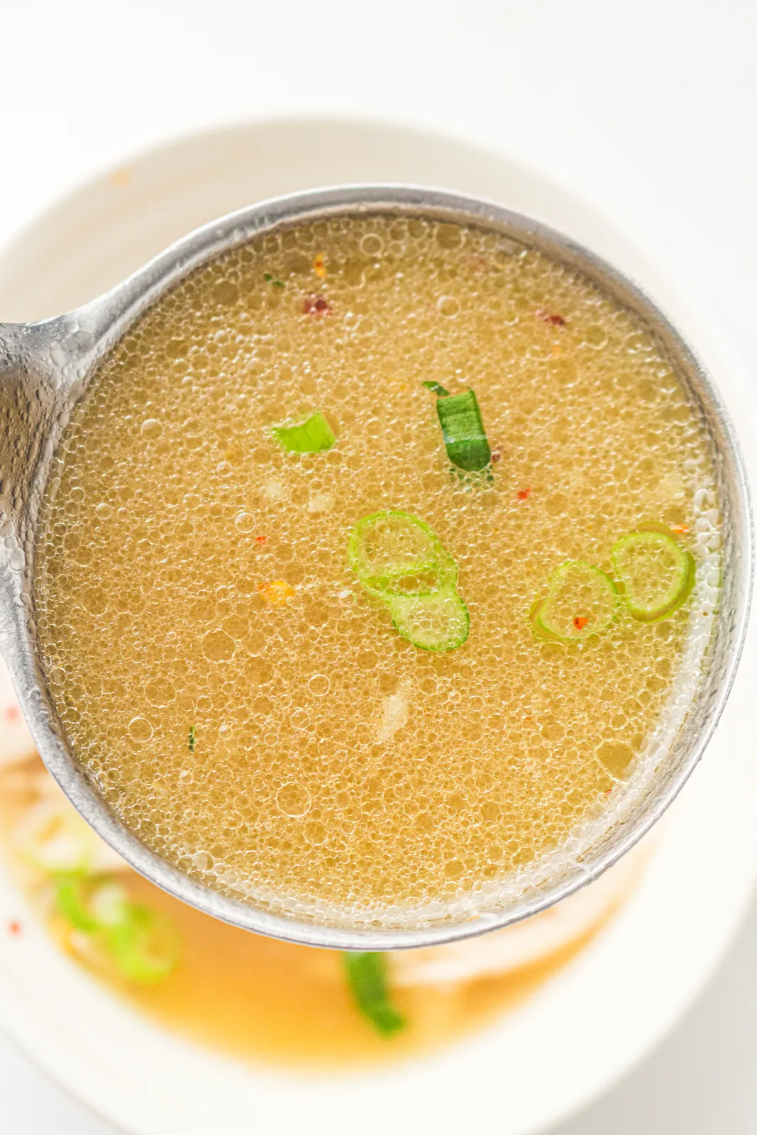 A ladle of golden broth held above a filled bowl