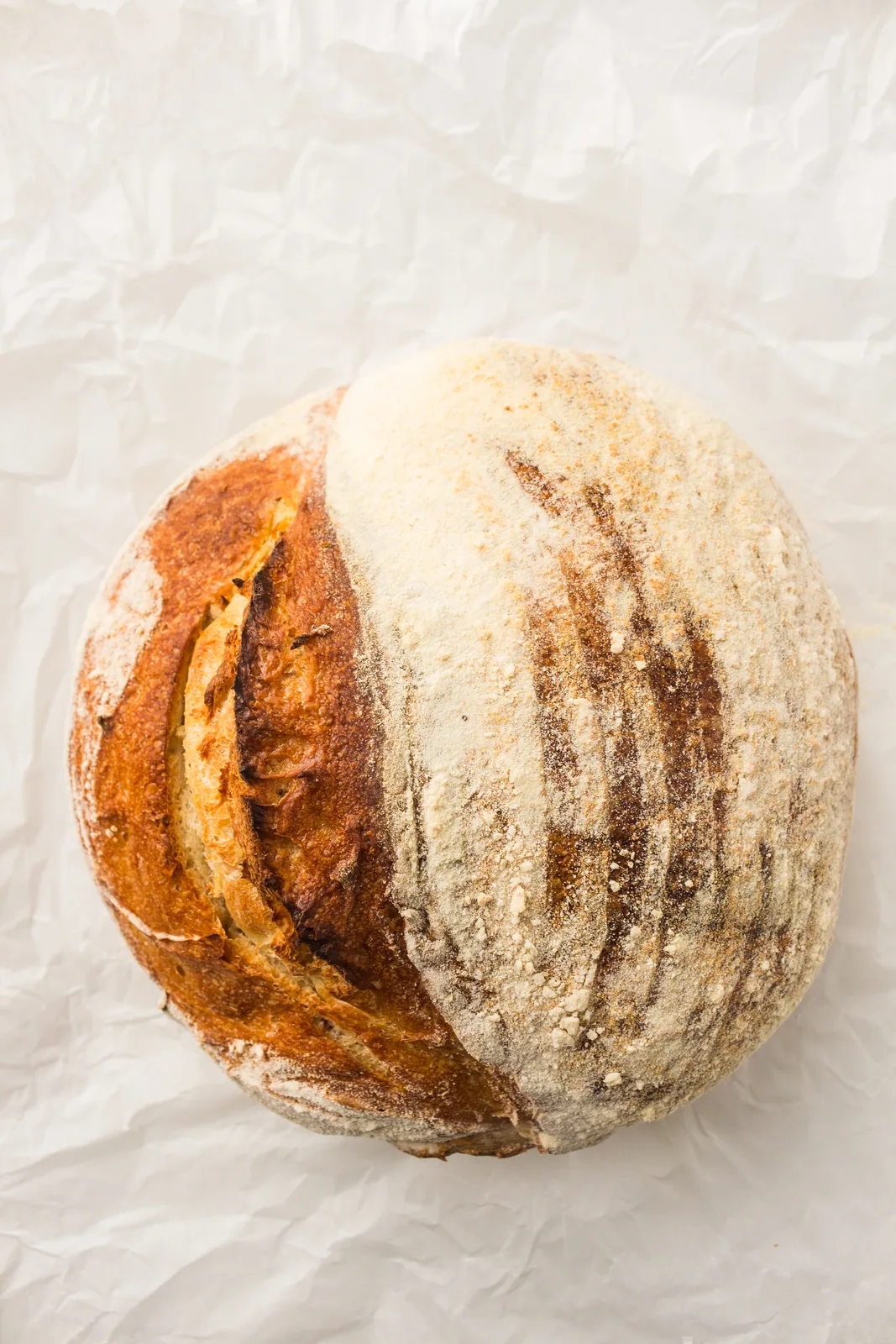 A scored artisan sourdough loaf photographed from above on parchment