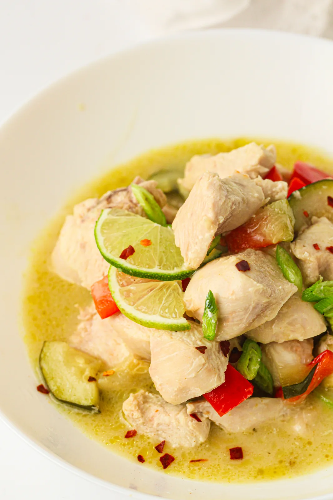 A white bowl of pale coconut sauce with lime slices and sliced chilli