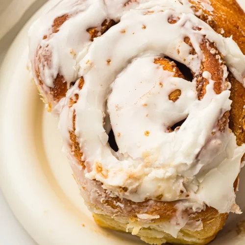 Bread machine cinnamon rolls glazed with vanilla icing, one bun on a white plate