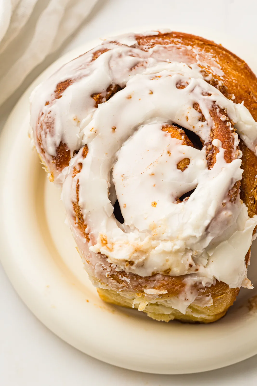 Bread machine cinnamon rolls glazed with vanilla icing, one bun on a white plate