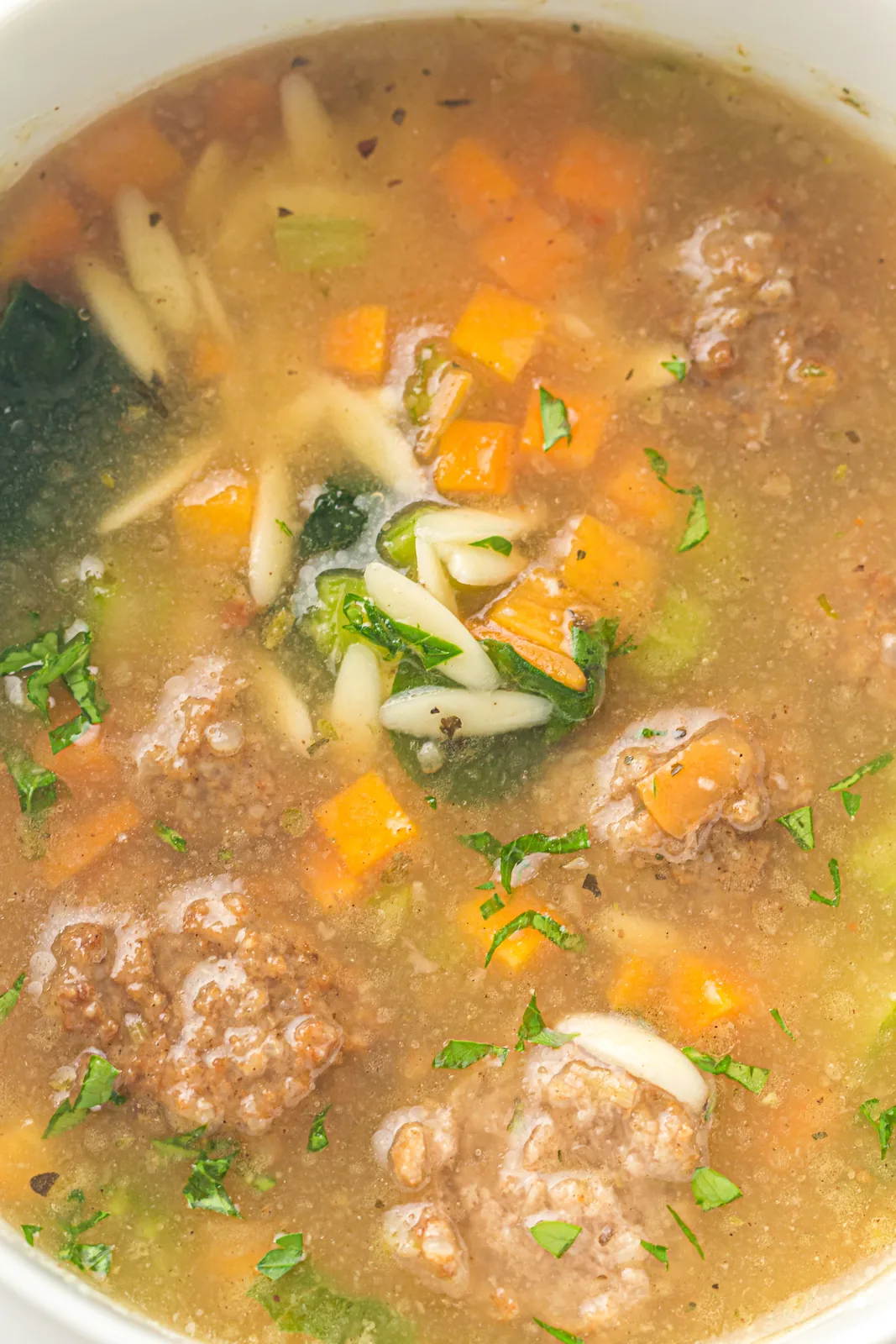 A brothy bowl with tiny meatballs, diced carrot and fresh herbs
