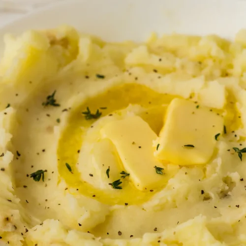 Buttery mashed potatoes in a white bowl with a pool of melted butter and fresh thyme