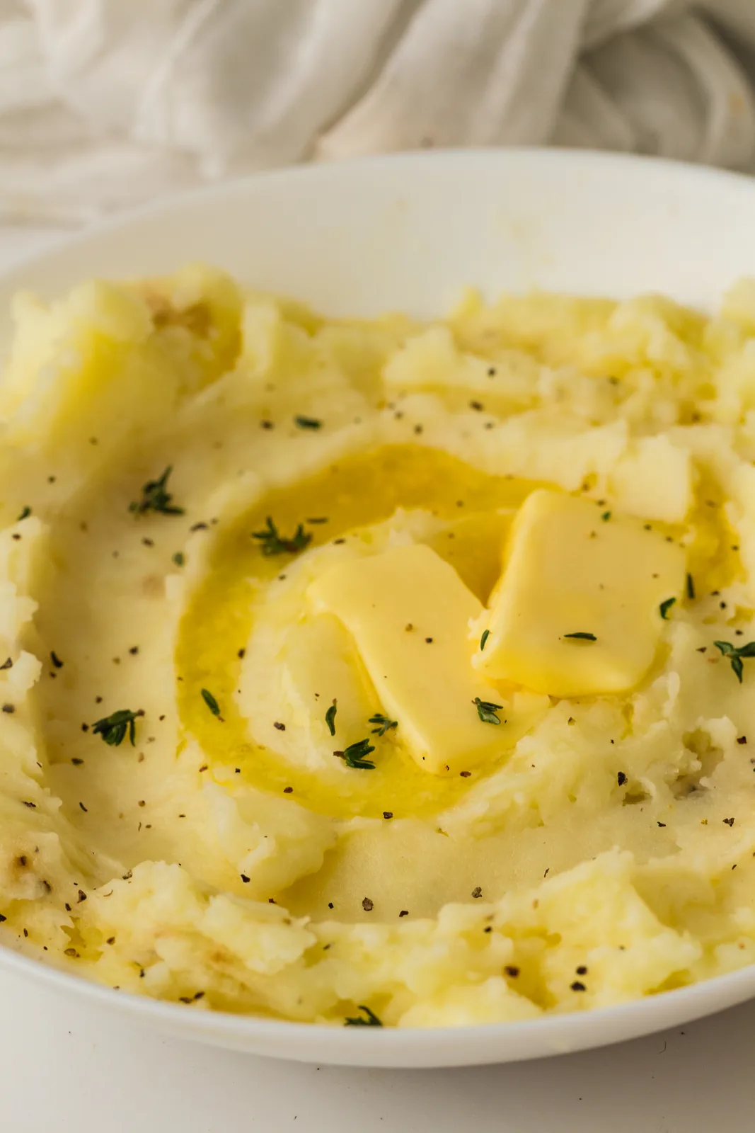 Buttery mashed potatoes in a white bowl with a pool of melted butter and fresh thyme