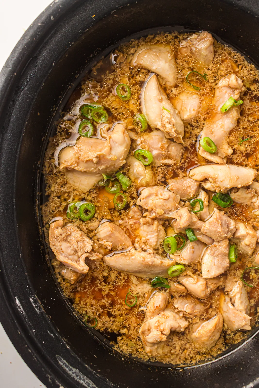 Tender pieces of meat sitting in a glossy amber sauce in the crock