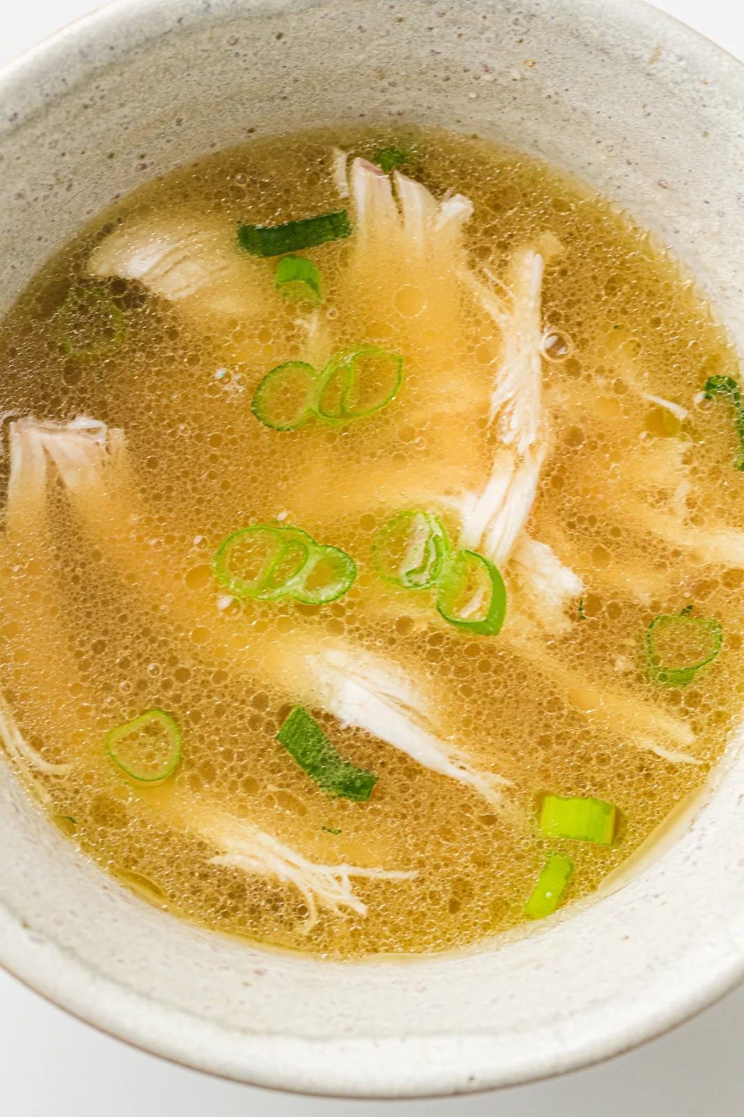 A bowl of chinese chicken soup with shredded meat and sliced scallions