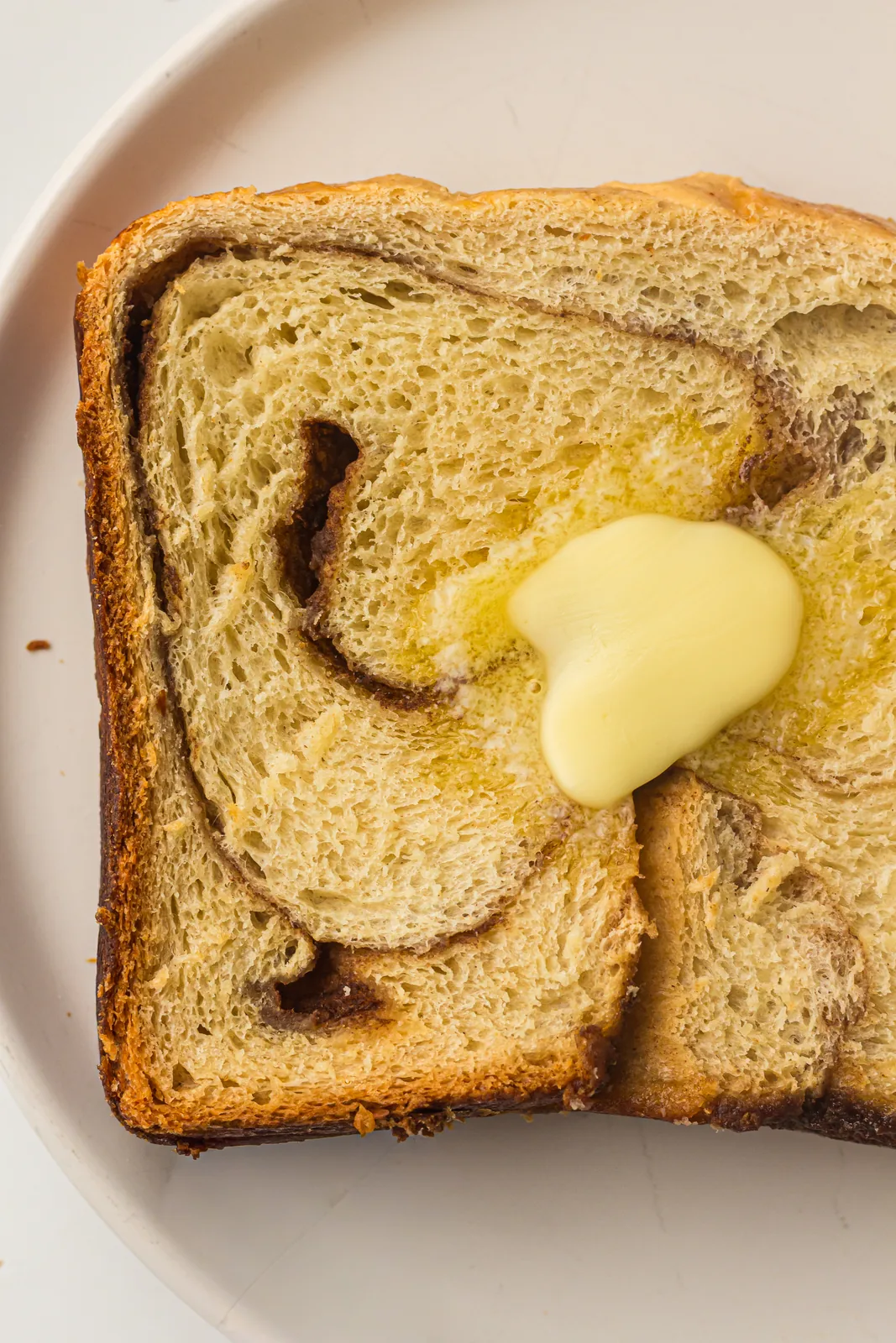 A warm slice on a white plate with a pat of butter melting into the spiral