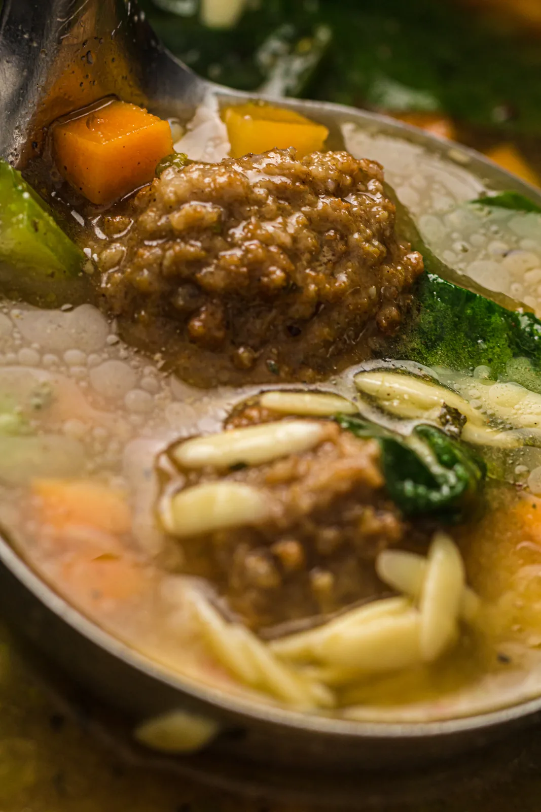 Close up of a small meatball and tiny pasta lifted on a spoon