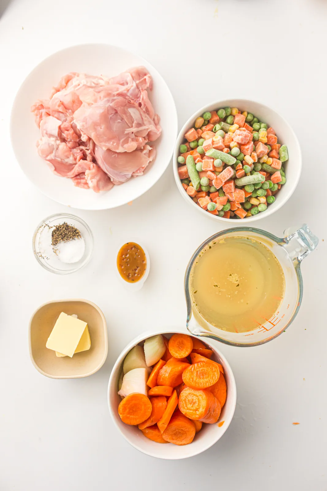 Ingredients for creamy chicken vegetable soup: chicken thighs, carrots, onion, frozen mixed vegetables, stock, butter and seasoning