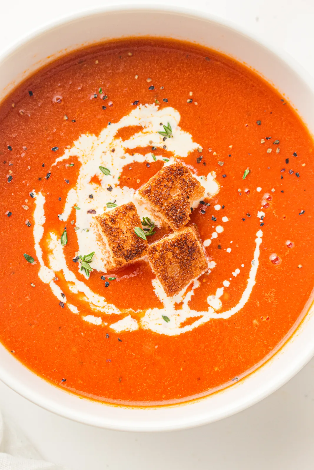 A bowl of creamy tomato soup with a swirl of cream and croutons