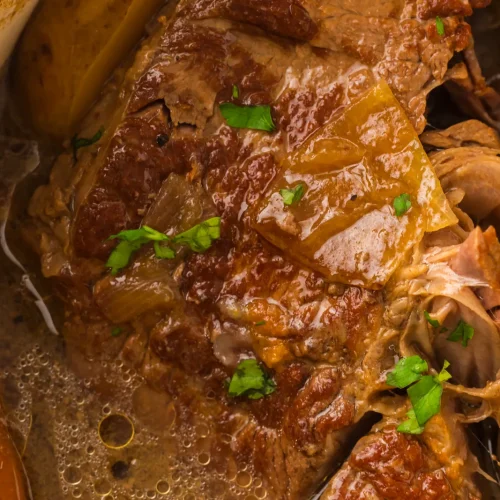 Dutch oven pot roast resting in its gravy with onions and parsley
