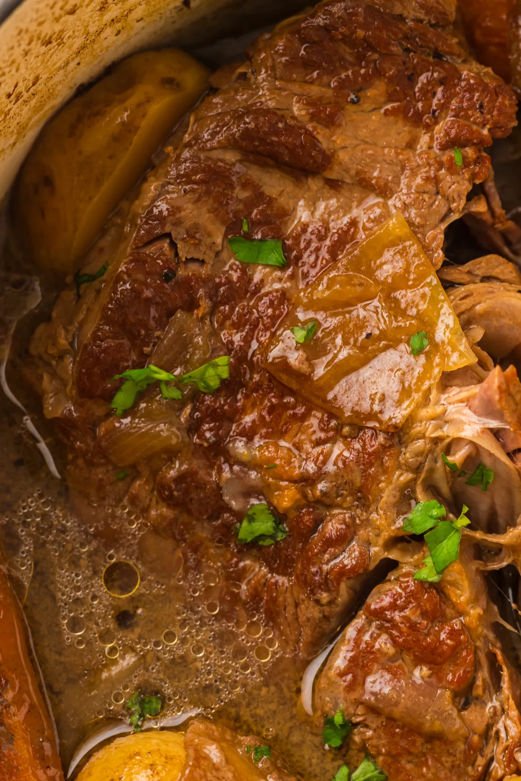 Dutch oven pot roast resting in its gravy with onions and parsley