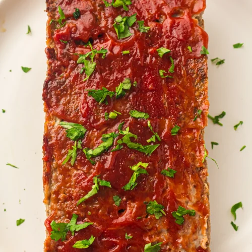Easy meatloaf glazed with ketchup and scattered with parsley on a white plate