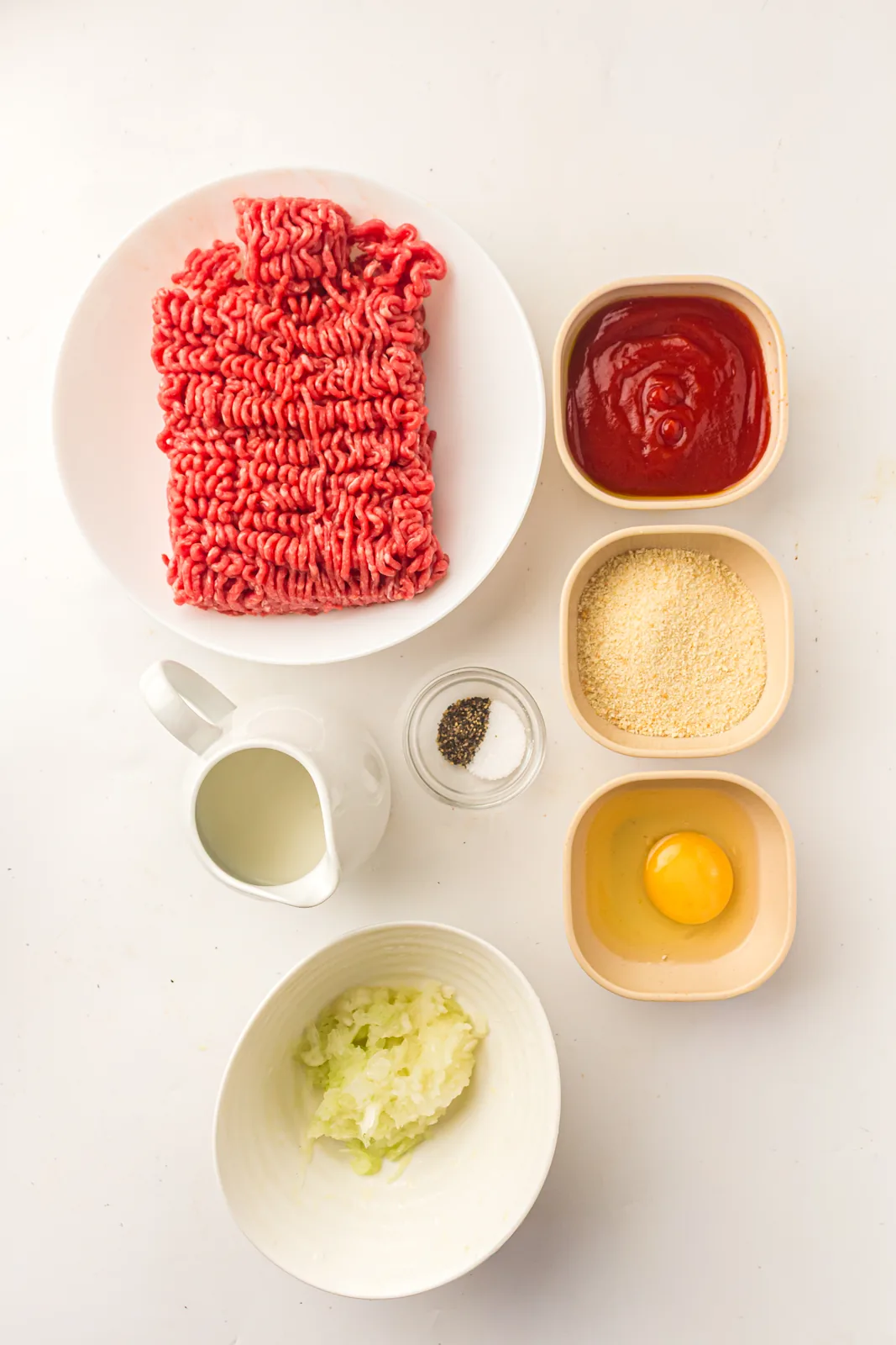 Ingredients for easy meatloaf: ground beef, breadcrumbs, milk, egg, grated onion and ketchup