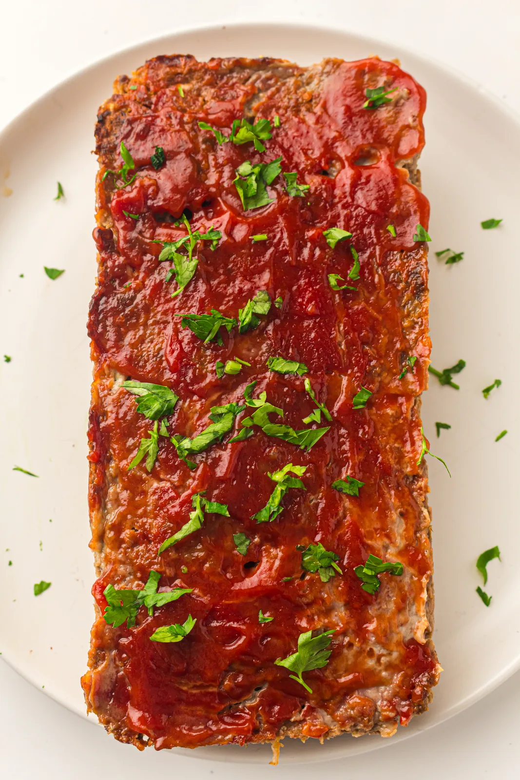 Easy meatloaf glazed with ketchup and scattered with parsley on a white plate