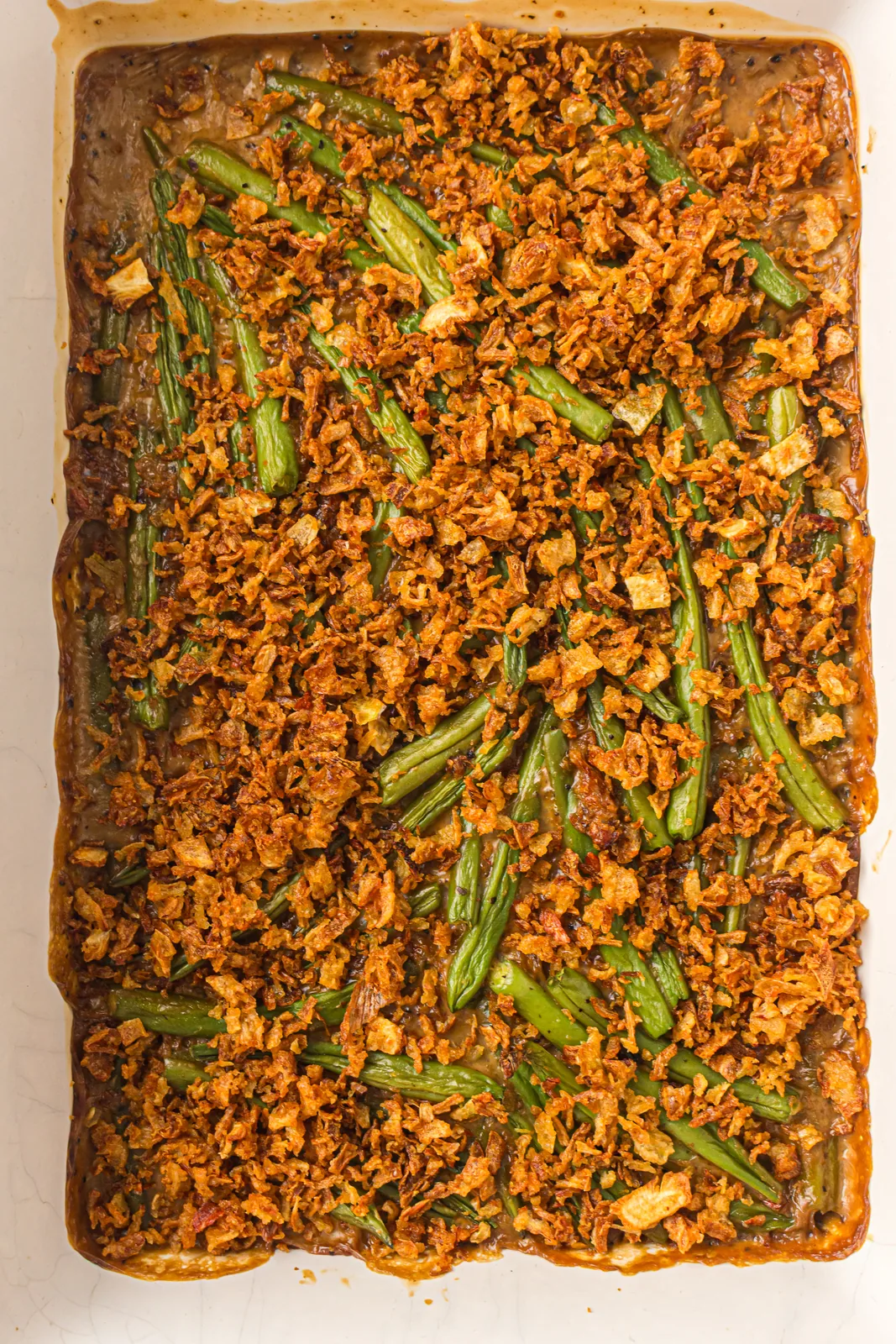 A baked fresh green bean casserole in a tray under a layer of crispy fried onions