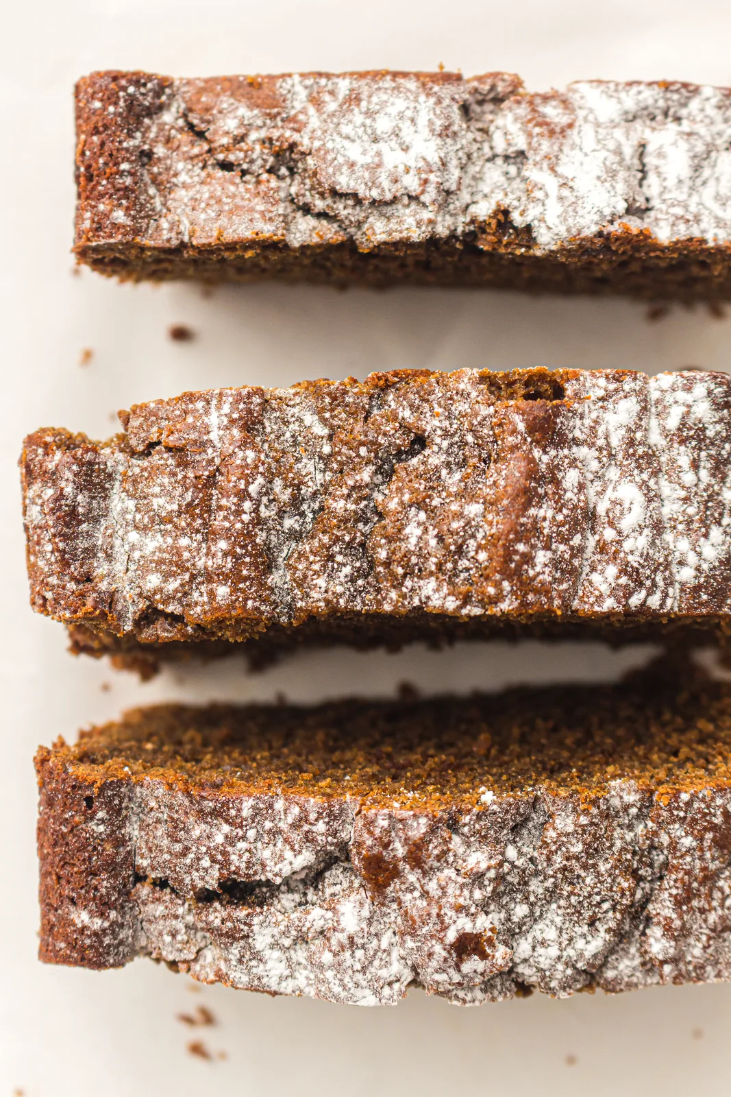 Thick slices of gingerbread loaf dusted with icing sugar and stacked on a board